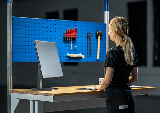 Eine Frau in Arbeitskleidung steht an einem ergonomischen Arbeitstisch.